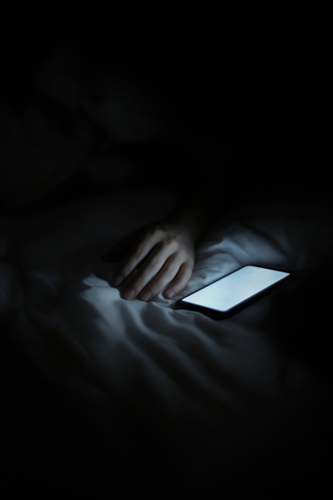 Mão sobre o lençol no escuro, iluminada só pela luz do celular